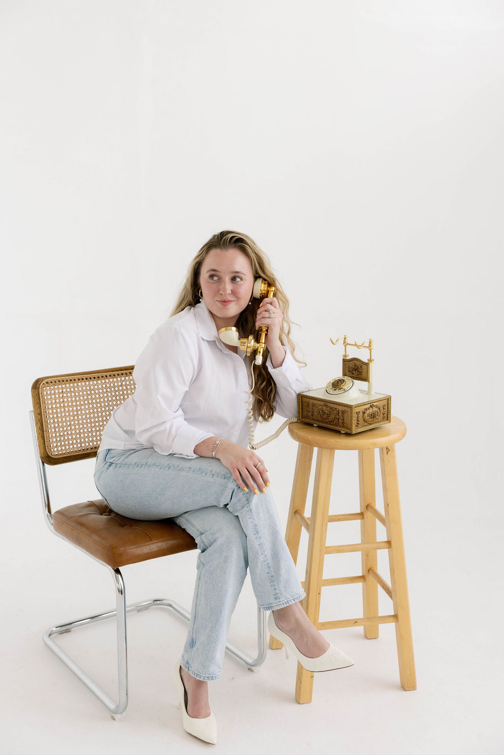 Woman sitting on a chair with a vintage phone, white background.