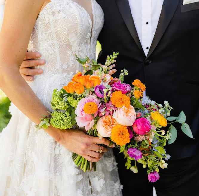 Bride and groom holding a vibrant 2026 wedding bouquet featuring garden roses, ranunculus, zinnias, viburnum, eucalyptus, and seasonal blooms with modern timeless floral design inspiration