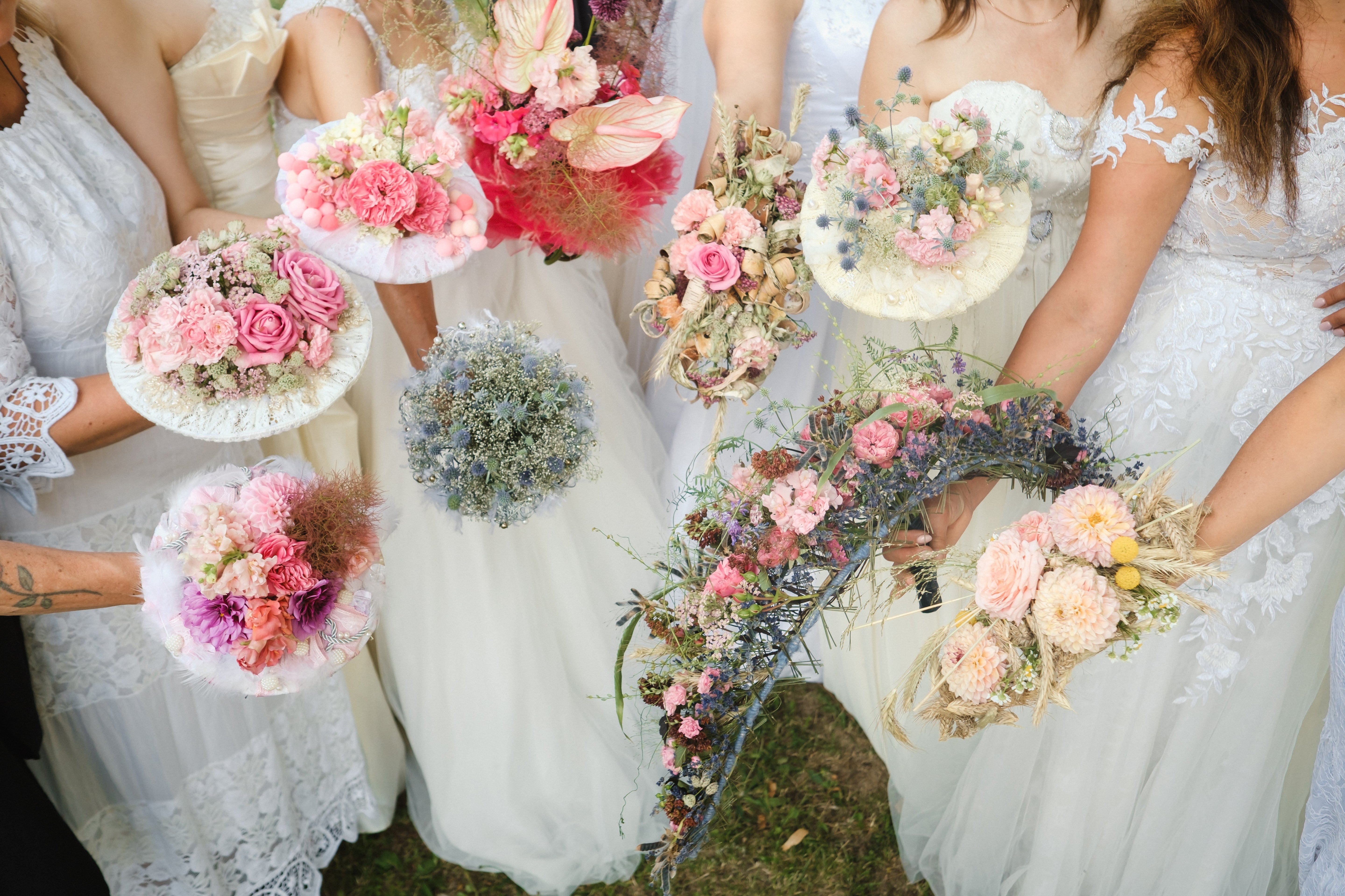 Multiple brides holding varying styles and sizes of flower bouquets.