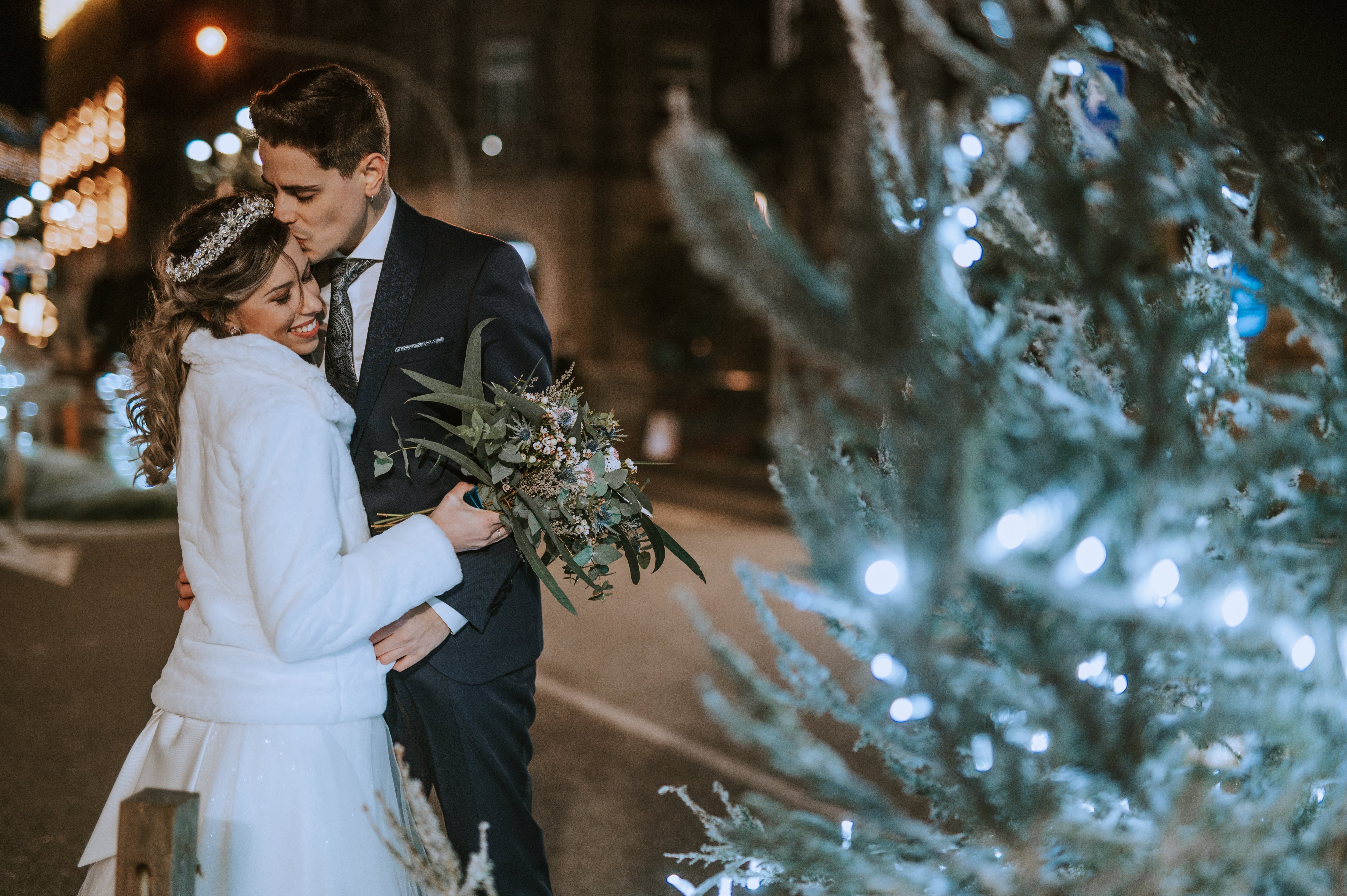 Winter bride bouquet featuring seasonal flowers including white roses, ranunculus, anemones, evergreen foliage, and winter berries.