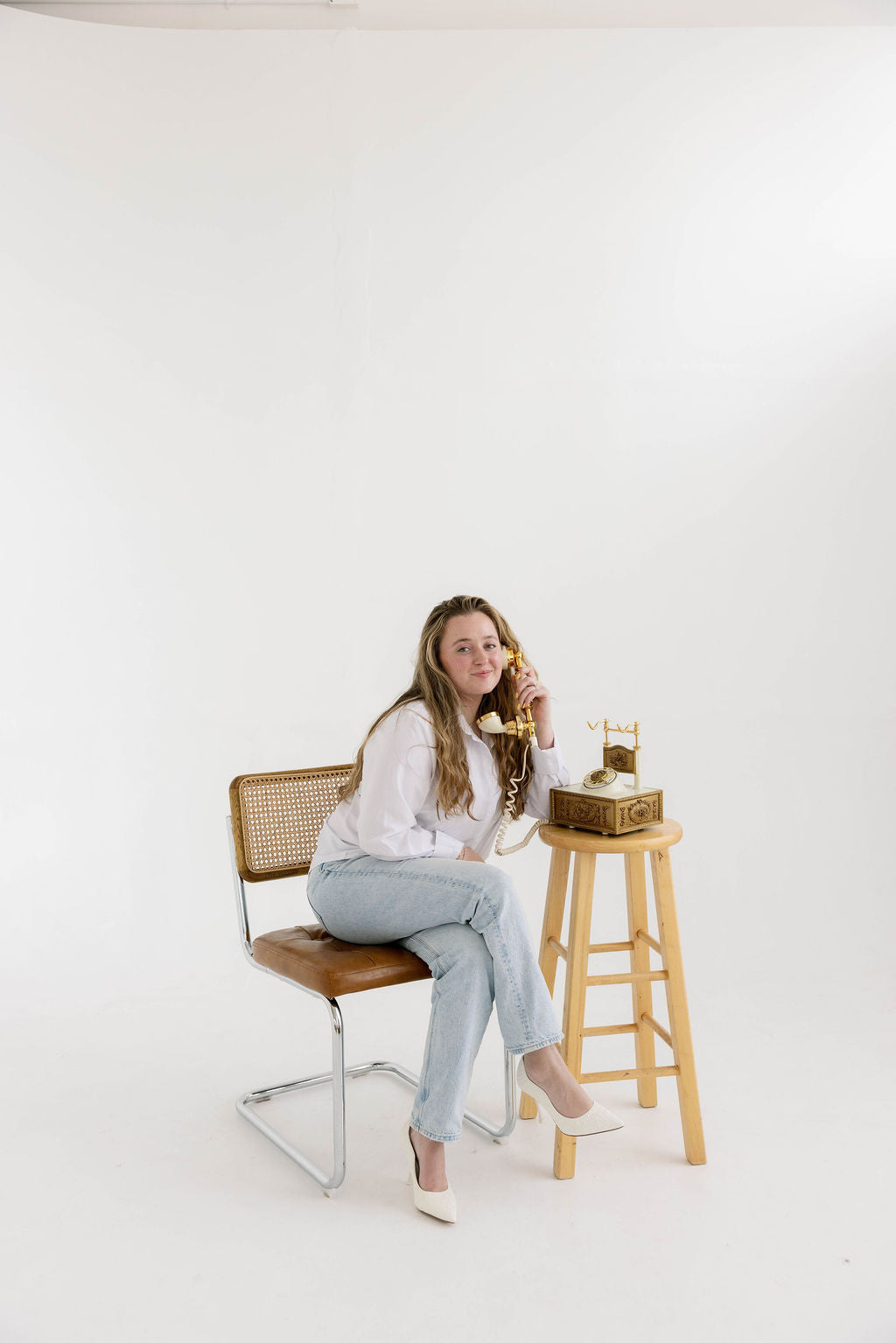 Blossom & Rhyme team member sitting on a chair with a wooden stool and old-fashioned telephone in a minimalistic setting.