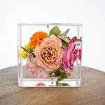 6x6 Resin Floral Block preserving a blush garden rose, pink rose, orange marigold, pink carnation, yellow daisy, eucalyptus, and delicate botanical accents in clear resin, handcrafted by Blossom & Rhymeblossomandrhyme