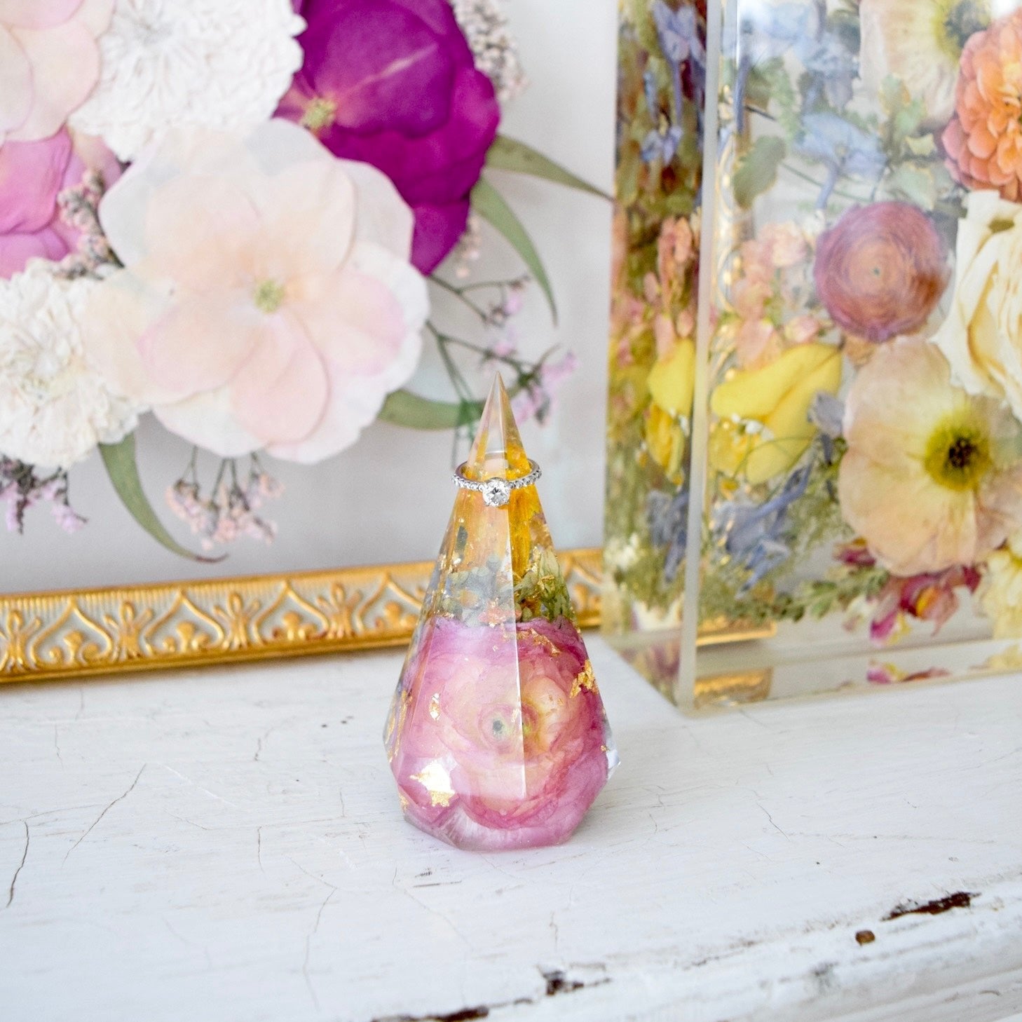 Faceted resin floral ring holder preserving blush pink ranunculus, soft greenery, and botanical accents with a diamond ring, handcrafted by Blossom & Rhyme