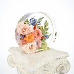 Custom small floral round preserving blush roses, blue delphiniums, orange blooms, and greenery in clear resin, handcrafted by Blossom & Rhyme