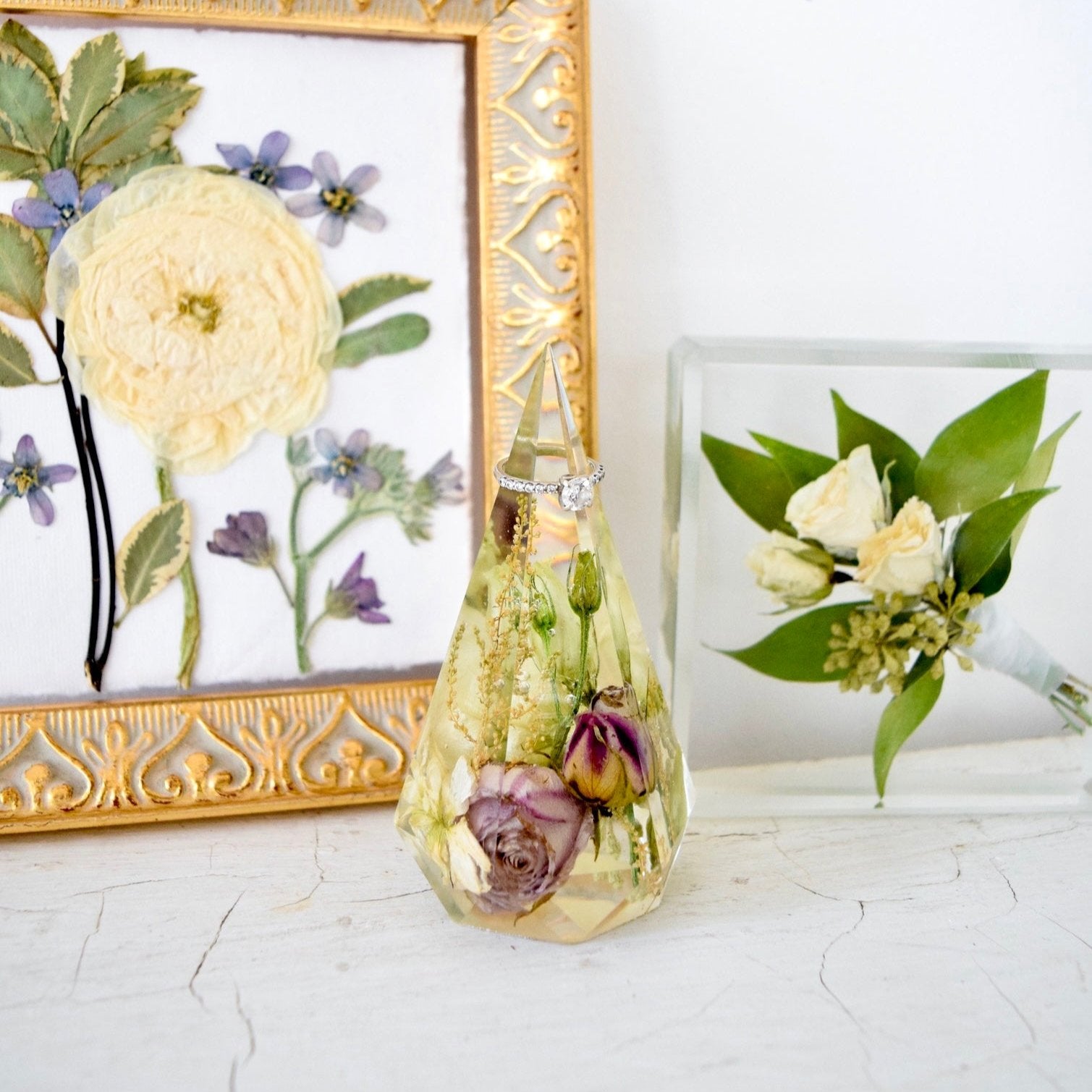 Faceted resin floral ring holder preserving lavender spray roses, white flower buds, baby's breath, and delicate botanical accents, displayed with a diamond ring and handcrafted by Blossom & Rhyme