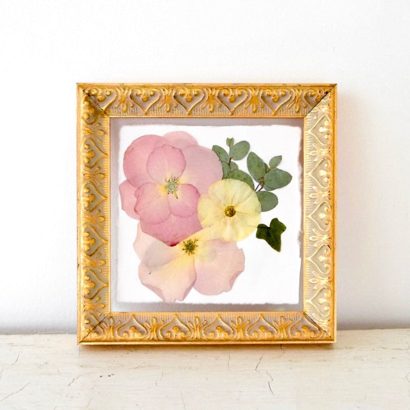 A gold-colored 6x6 pressed frame containing pink and yellow flowers with green leaves, displayed on a white surface