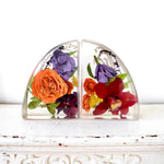 Small resin bookends preserving orange garden roses, burgundy orchids, purple hydrangeas, yellow yarrow, pansies, and botanical greenery in clear resin, handcrafted by Blossom & Rhyme
