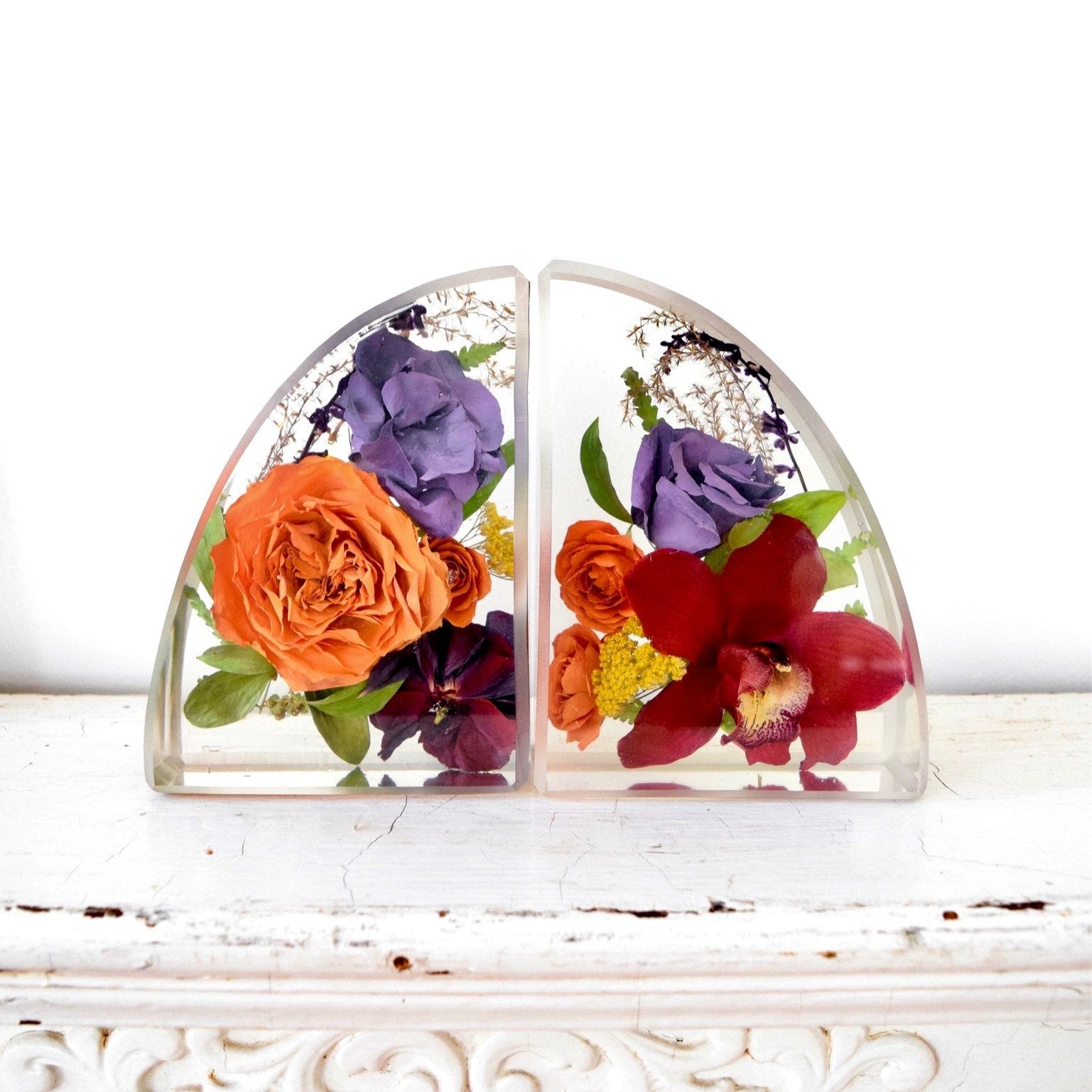 Small resin bookends preserving orange garden roses, burgundy orchids, purple hydrangeas, yellow yarrow, pansies, and botanical greenery in clear resin, handcrafted by Blossom & Rhyme