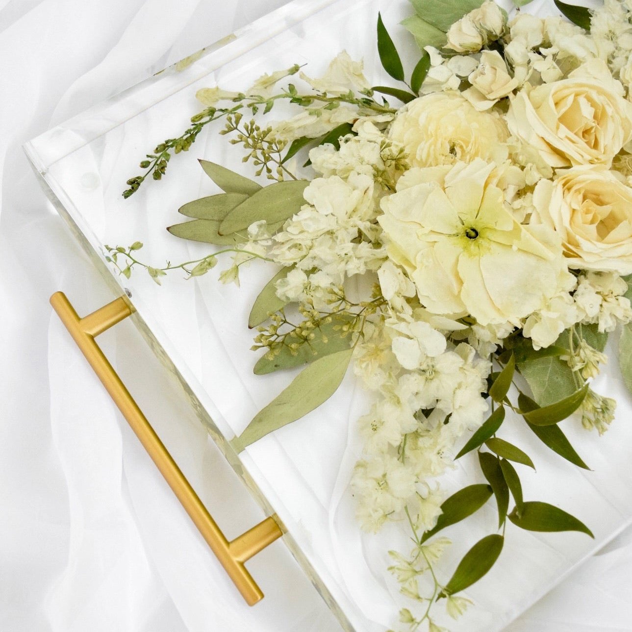 Close-up of a resin floral tray preserving ivory roses, white hydrangeas, ranunculus, stock flowers, eucalyptus, olive leaves, and delicate greenery in clear resin, handcrafted by Blossom & Rhyme