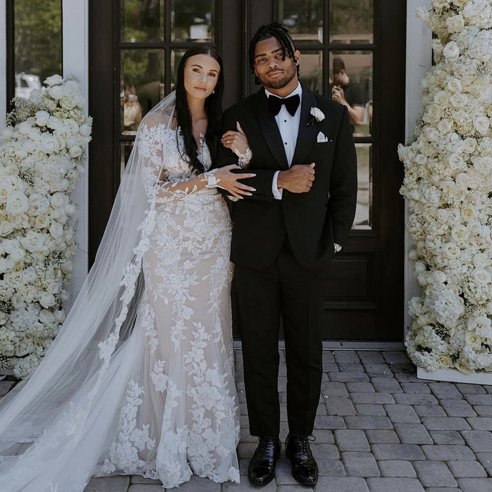 Bride and groom posing together on their wedding day in front of white floral installations before preserving their wedding bouquet with Blossom & Rhyme