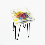 A square side table with a resin top featuring a floral design and a depth of up to 4 inches, supported by metal hairpin legs.